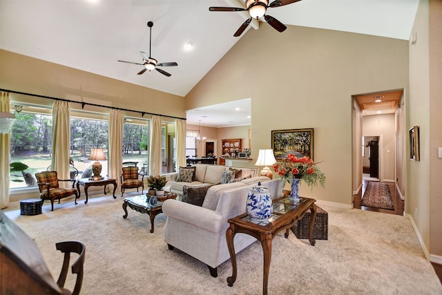 carpeted living room with high vaulted ceiling and ceiling fan with notable chandelier