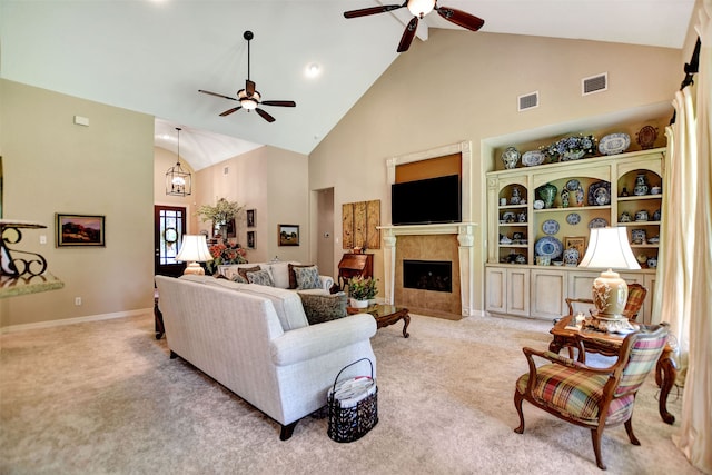 carpeted living room featuring a tiled fireplace, high vaulted ceiling, and ceiling fan with notable chandelier