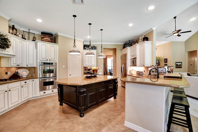 kitchen featuring kitchen peninsula, pendant lighting, white cabinets, built in appliances, and a breakfast bar area