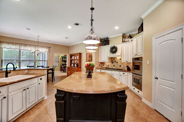 kitchen with sink, hanging light fixtures, crown molding, a chandelier, and a center island with sink