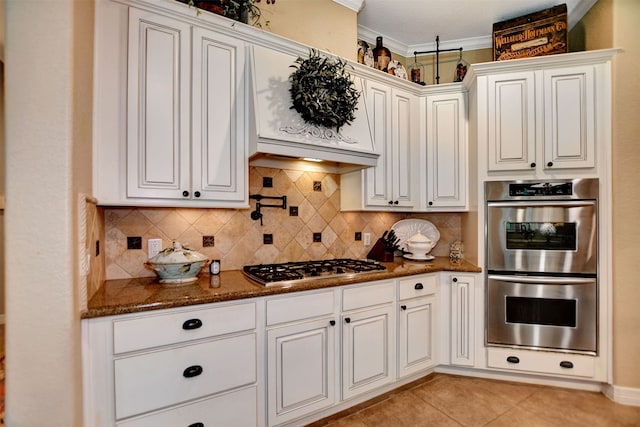 kitchen featuring decorative backsplash, white cabinets, light tile patterned floors, dark stone counters, and stainless steel appliances