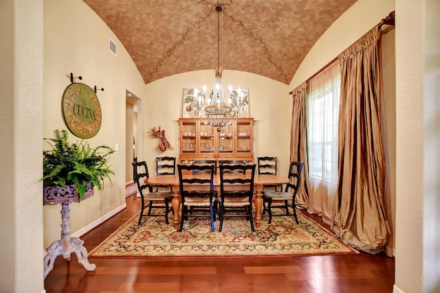 dining space with wood-type flooring, lofted ceiling, and an inviting chandelier