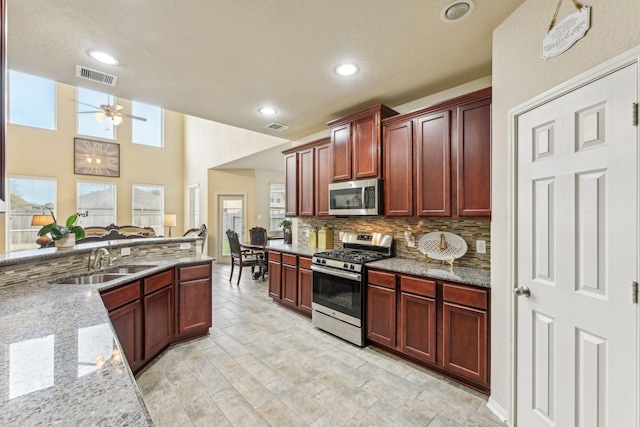 kitchen with stainless steel appliances, ceiling fan, sink, backsplash, and light stone counters