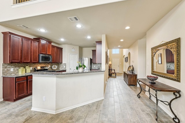 kitchen featuring kitchen peninsula, appliances with stainless steel finishes, tasteful backsplash, light wood-type flooring, and dark stone counters