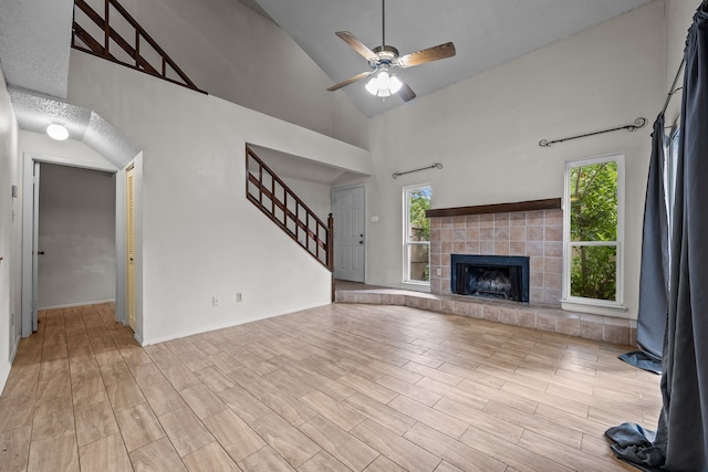 unfurnished living room featuring high vaulted ceiling, a tile fireplace, light wood-type flooring, and ceiling fan