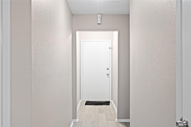 corridor featuring light wood-type flooring and a textured ceiling