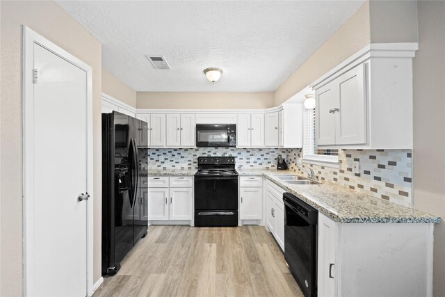 kitchen with light stone countertops, white cabinetry, sink, black appliances, and light wood-type flooring