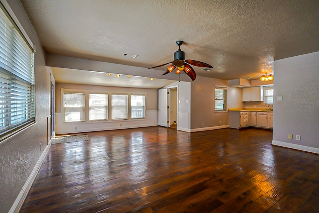 unfurnished living room with sink, dark wood-type flooring, a textured ceiling, and ceiling fan with notable chandelier