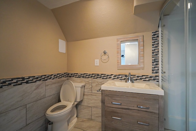 bathroom with lofted ceiling, toilet, vanity, tile walls, and walk in shower