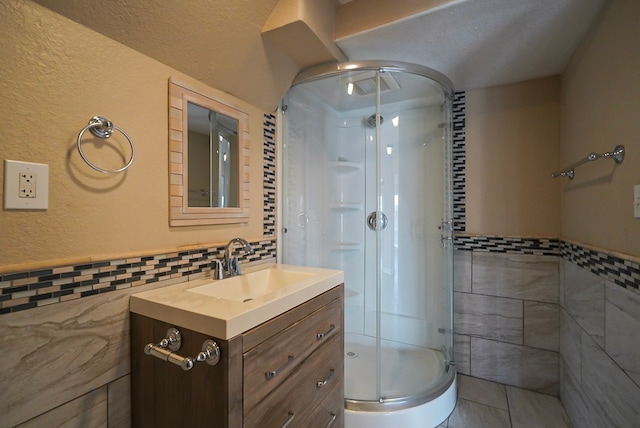 bathroom featuring a shower with door, a textured ceiling, tile walls, vanity, and tile patterned flooring