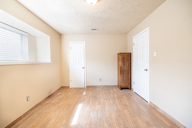 empty room with a textured ceiling and light hardwood / wood-style flooring