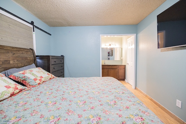 bedroom featuring light hardwood / wood-style flooring, a textured ceiling, a barn door, and ensuite bathroom