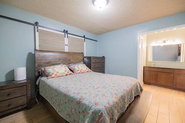 bedroom with a barn door, a textured ceiling, and light wood-type flooring