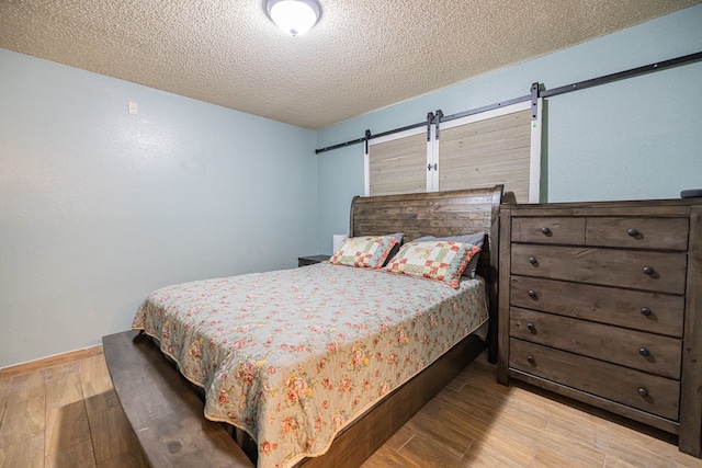 bedroom with a textured ceiling, a barn door, and light wood-type flooring