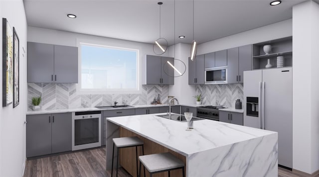 kitchen featuring an island with sink, sink, appliances with stainless steel finishes, light stone counters, and tasteful backsplash