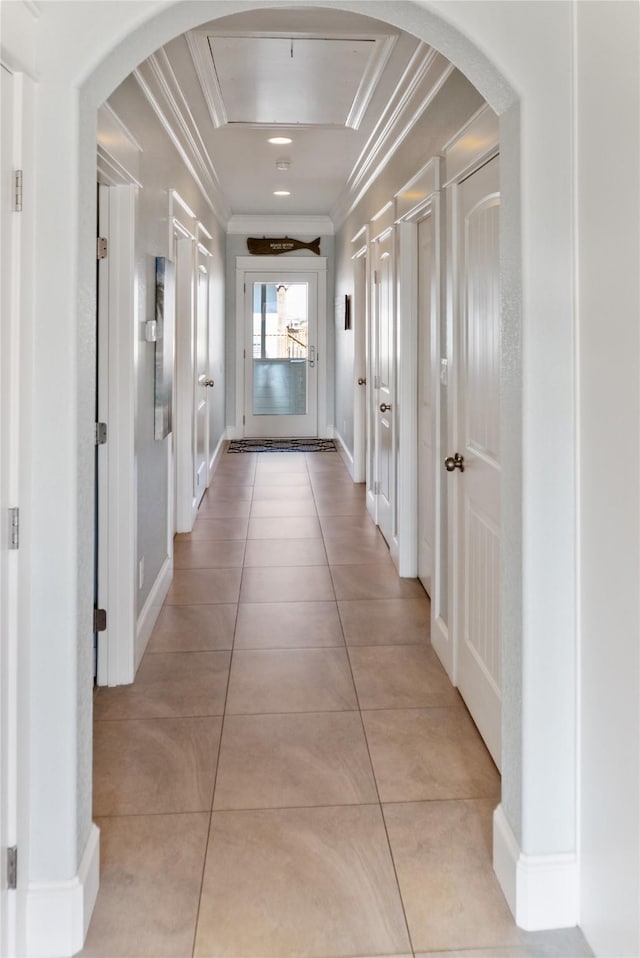 corridor featuring crown molding, light tile patterned floors, baseboards, and arched walkways