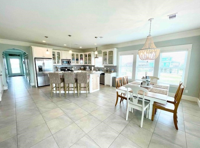 dining area featuring arched walkways, visible vents, plenty of natural light, and ornamental molding