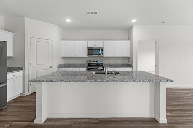 kitchen featuring a center island with sink, visible vents, light stone counters, stainless steel appliances, and a sink