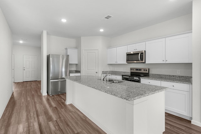 kitchen with a center island with sink, white cabinets, dark wood finished floors, appliances with stainless steel finishes, and a sink