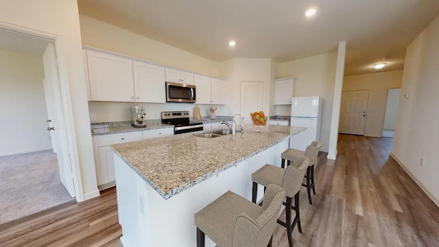 kitchen with light stone countertops, sink, stainless steel appliances, white cabinets, and a center island with sink