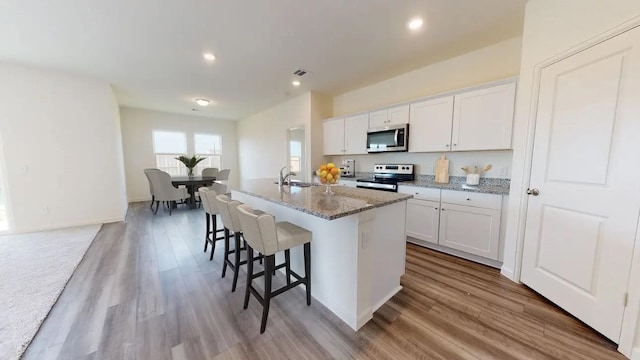 kitchen with a breakfast bar, stainless steel appliances, white cabinets, a sink, and an island with sink