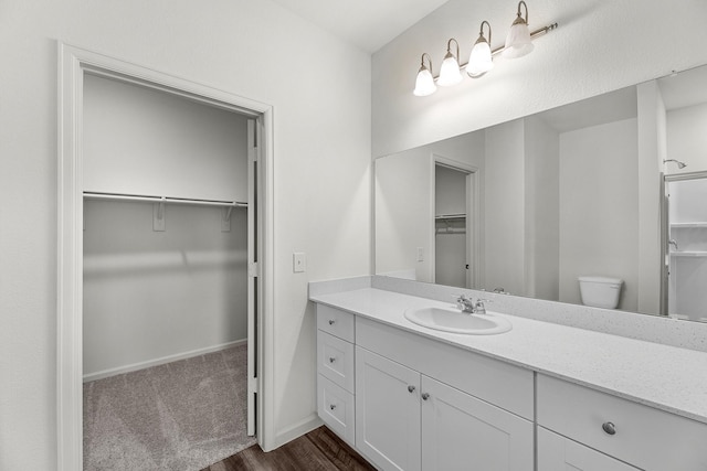 full bath with a walk in closet, toilet, vanity, and baseboards