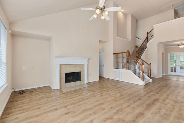 unfurnished living room with a tiled fireplace, high vaulted ceiling, and light wood-type flooring