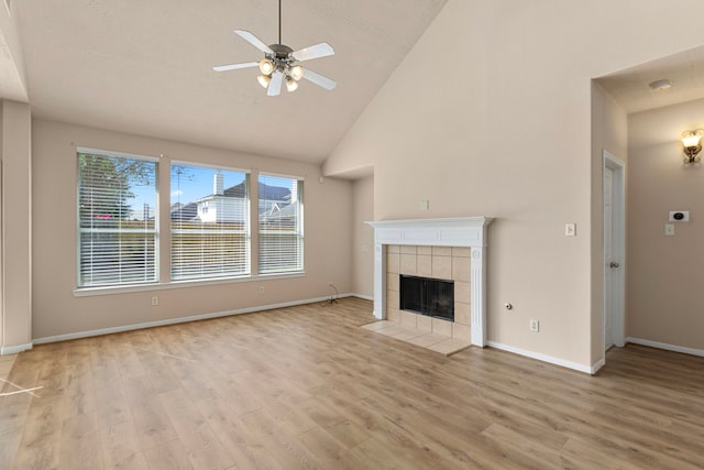 unfurnished living room with a tiled fireplace, ceiling fan, a textured ceiling, high vaulted ceiling, and light hardwood / wood-style flooring