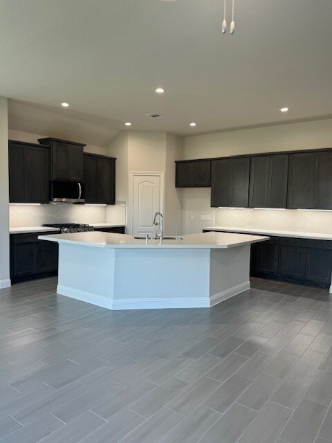 kitchen with light hardwood / wood-style flooring, sink, a center island with sink, and backsplash