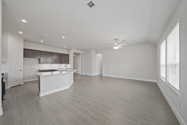 kitchen featuring dark brown cabinetry, lofted ceiling, light hardwood / wood-style flooring, ceiling fan, and a kitchen island with sink