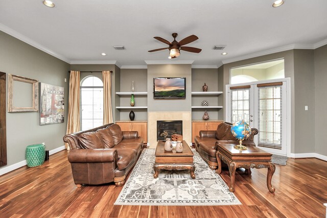 living room with crown molding, ceiling fan, wood-type flooring, and a tile fireplace