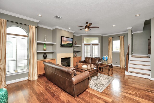 living room with dark wood-type flooring, ornamental molding, built in shelves, and a textured ceiling