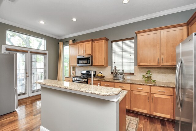 kitchen featuring crown molding, appliances with stainless steel finishes, dark hardwood / wood-style floors, a center island, and light stone countertops