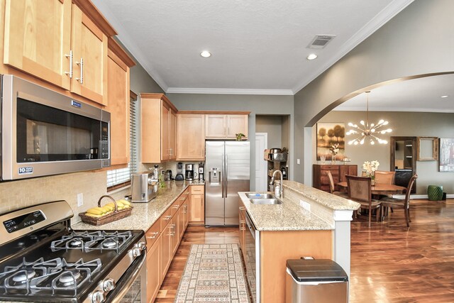 kitchen with sink, appliances with stainless steel finishes, hanging light fixtures, light stone countertops, and an island with sink