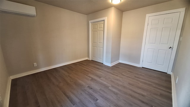 unfurnished bedroom featuring dark hardwood / wood-style flooring and a wall unit AC