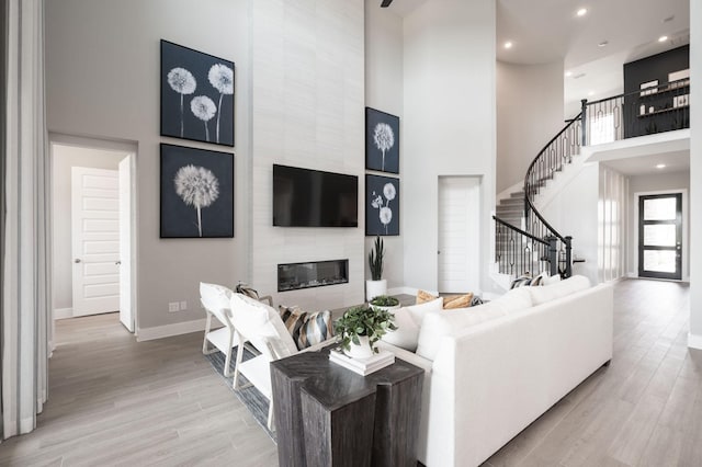 living room featuring a towering ceiling, a tile fireplace, and light wood-type flooring