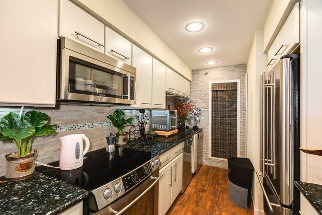 kitchen with backsplash, white cabinetry, stainless steel appliances, dark stone countertops, and dark hardwood / wood-style floors