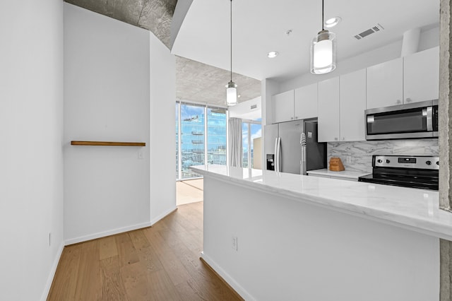 kitchen featuring hanging light fixtures, stainless steel appliances, light stone counters, backsplash, and white cabinets