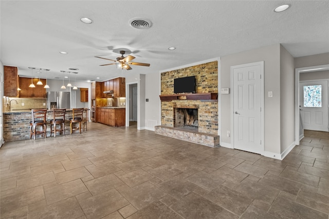 unfurnished living room featuring a textured ceiling, a fireplace, ceiling fan, and sink