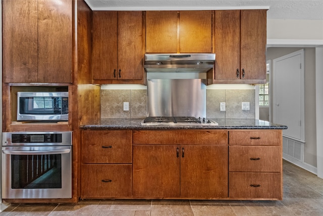 kitchen featuring dark stone countertops, a textured ceiling, backsplash, and appliances with stainless steel finishes