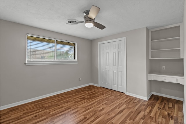 unfurnished bedroom with built in desk, ceiling fan, a textured ceiling, hardwood / wood-style floors, and a closet