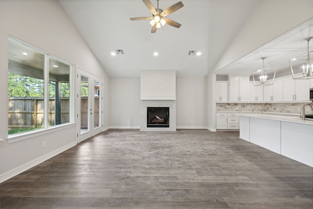 unfurnished living room with visible vents, dark wood-style flooring, ceiling fan with notable chandelier, and a fireplace