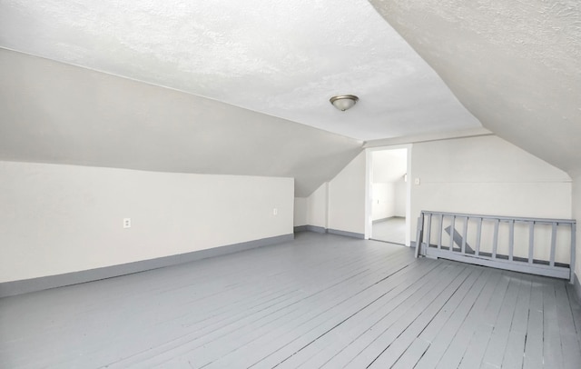 additional living space with a textured ceiling, vaulted ceiling, and hardwood / wood-style flooring