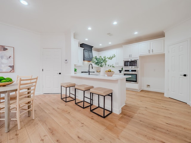 kitchen featuring white cabinets, light wood-type flooring, ornamental molding, a kitchen bar, and stainless steel appliances