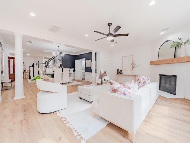 living room featuring ceiling fan with notable chandelier, a large fireplace, ornate columns, and light hardwood / wood-style flooring