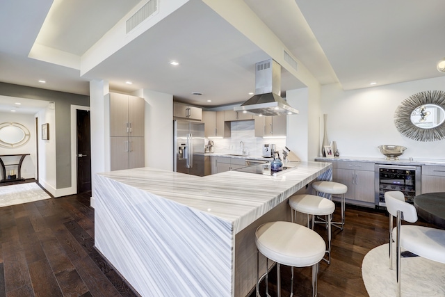 kitchen featuring a kitchen bar, island exhaust hood, kitchen peninsula, beverage cooler, and stainless steel refrigerator with ice dispenser