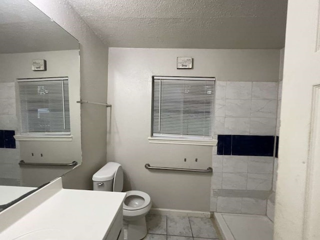 bathroom with a textured ceiling, walk in shower, toilet, vanity, and tile patterned flooring