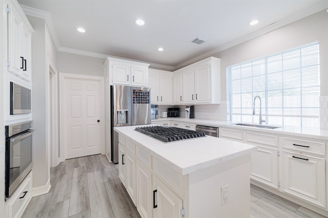 kitchen with appliances with stainless steel finishes, white cabinetry, sink, and a kitchen island