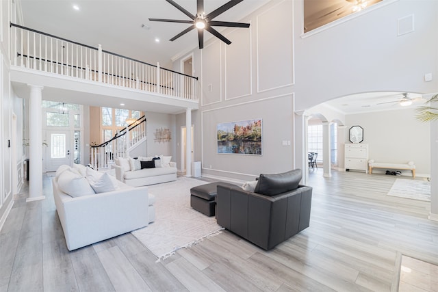 living room featuring decorative columns, light hardwood / wood-style floors, a towering ceiling, and ceiling fan