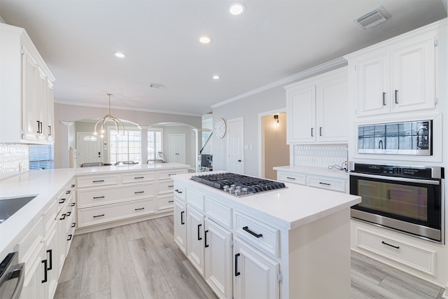 kitchen with hanging light fixtures, kitchen peninsula, white cabinetry, appliances with stainless steel finishes, and tasteful backsplash